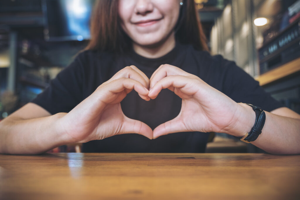 A smiley face Asian woman making heart hand sign with feeling inlove