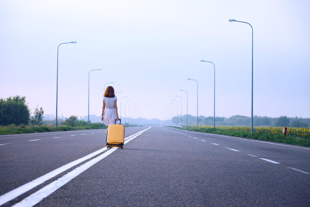 problems in the journey. the girl goes along the dividing strip with a yellow suitcase on the side of the road