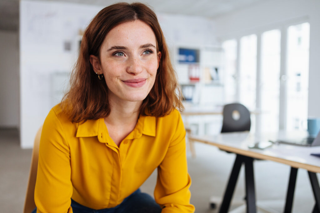 Young woman taking a break in the office sitting daydreaming looking up with a faraway expression and sweet smile