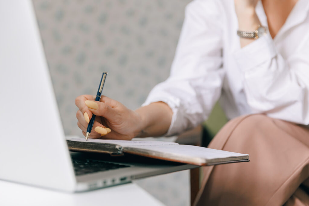 Closeup woman psychotherapist is holding notebook and making notes during online therapy session, background internet laptop with web call.